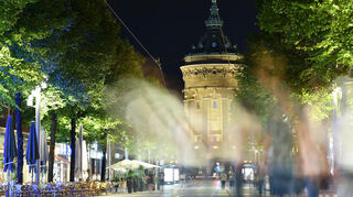 Menschen gehen am späten Abend in der Fußgängerzone der Innenstadt vor dem Wasserturm.