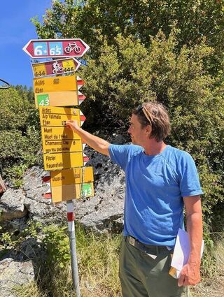 Wanderführer Georg Pawlata markiert ein Wegeschild im Unterengandin mit einem "Ü" für Überquerung.