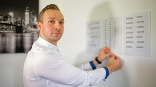 Nicolas Will klebt in seiner Wohnung bedruckte Seiten mit Übungswörtern an eine Wand.