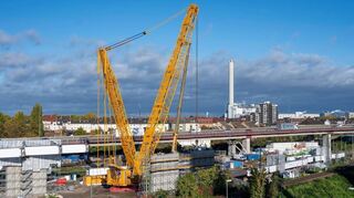Neben dem riesigen Kran sind die bereits betonierten Pfeiler der künftigen Brücke zu sehen. Im Hintergrund verläuft die Hochstraße Nord.
