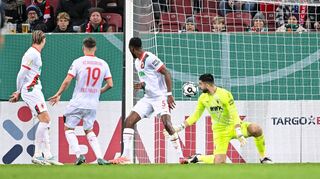 Der Schuss, der zum Augsburger Pokal-K.o. führt. Verteidiger Chrislain Matsima (M) fälscht den Ball auch noch unglücklich und damit unhaltbar ab.