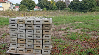 Ein Bild aus dem September 2025: Das Baugelände ist vorbereitet. Bauzaunfüße stehen gestapelt auf dem Gelände. Einsam lehnen lässig ein paar Bauzäune am Baum und warten auf ihren Einsatz.