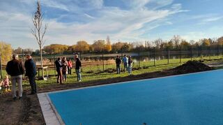 Basketballfeld und Badesee sind durch Zaun und Bepflanzung voneinander getrennt.